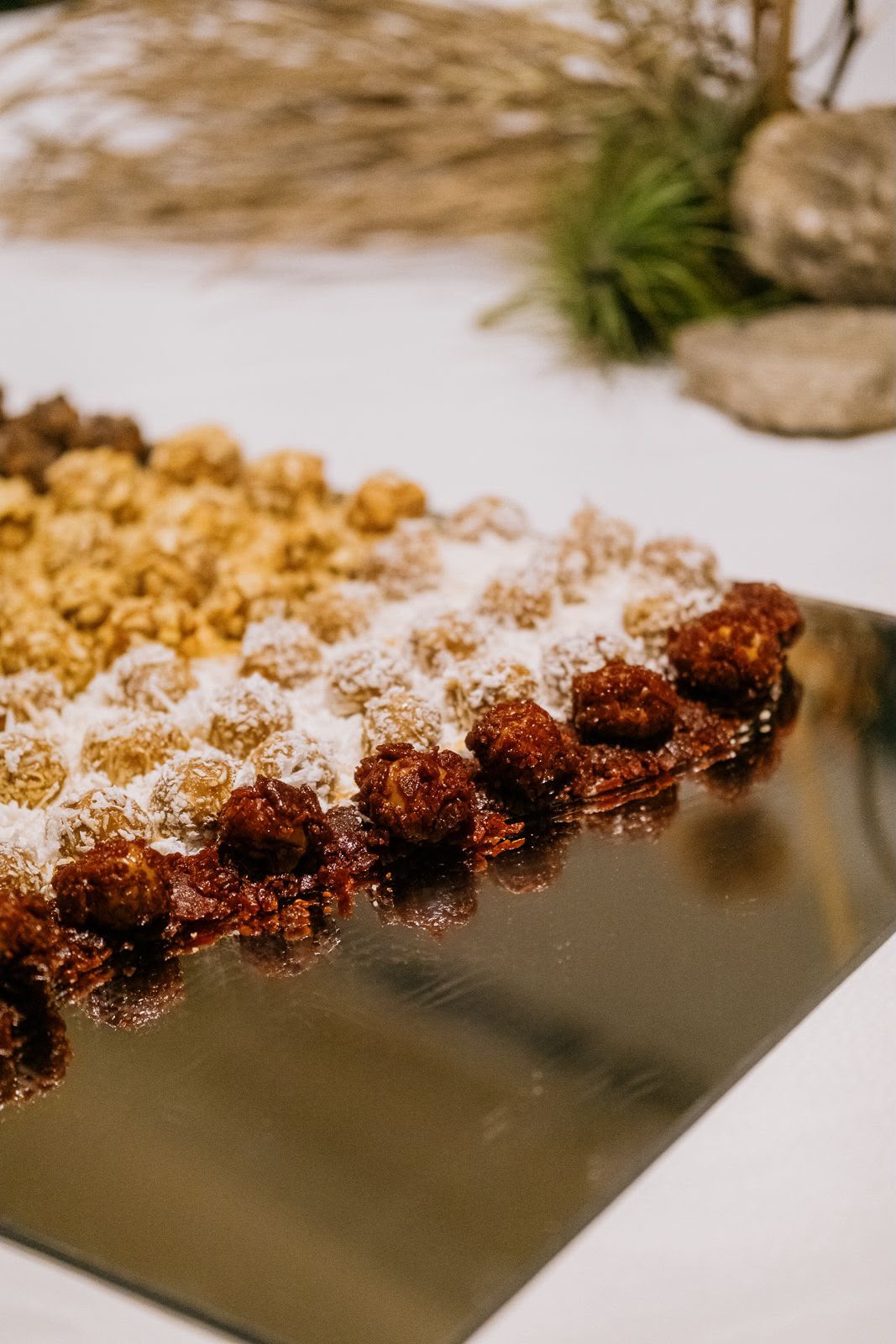 Fileiras de doces cobertos com coco e castanhas sobre travessa espelhada.